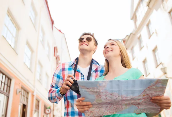 Sonriente pareja con mapa y cámara de fotos en la ciudad — Foto de Stock