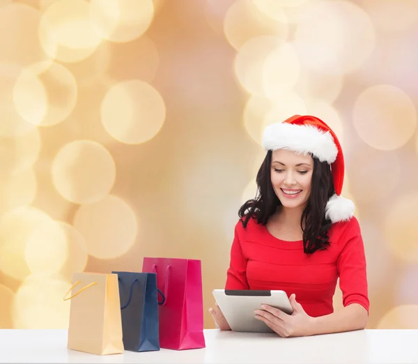 Donna sorridente in cappello di Babbo Natale con borse e tablet pc — Foto Stock