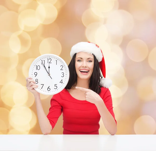 Femme souriante dans santa chapeau d'aide avec horloge — Photo