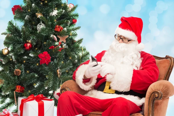 Santa claus com smartphone e árvore de natal — Fotografia de Stock