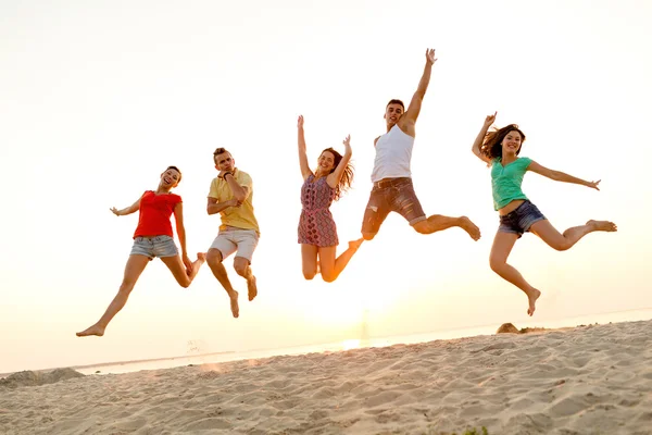 Lächelnde Freunde tanzen und springen am Strand — Stockfoto