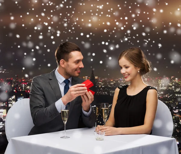 Smiling couple with red gift box at restaurant — Stock Photo, Image