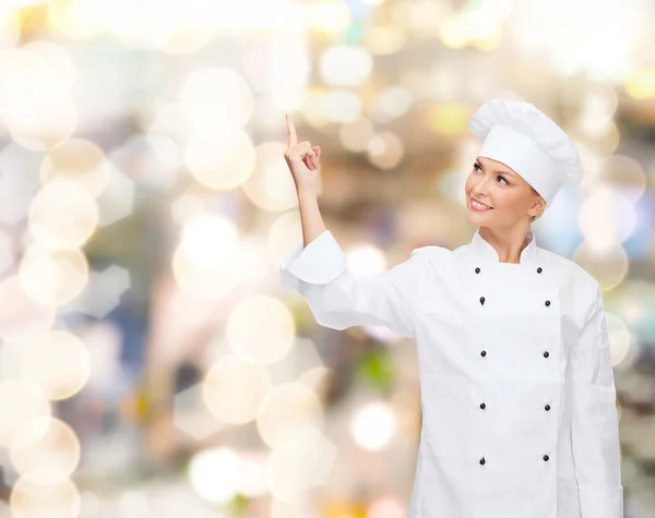 Uśmiechnięta kobieta kucharz palcem wskazującym na coś — Zdjęcie stockowe