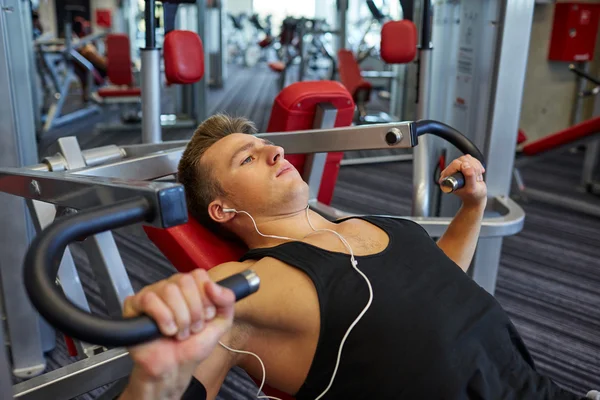 Young man with earphones exercising on gym machine — Stock Photo, Image