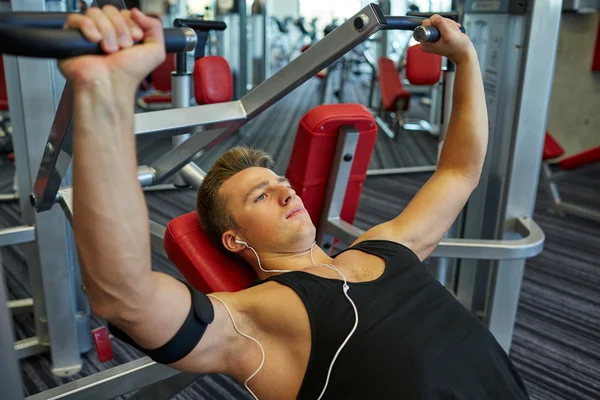 Joven con auriculares ejercitándose en la máquina de gimnasio — Foto de Stock