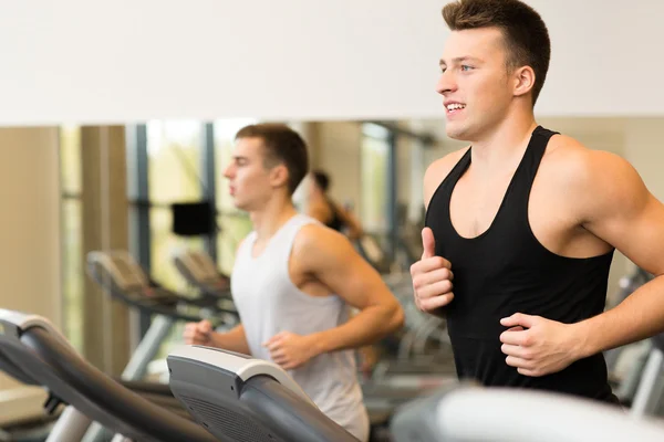 Lächelnde Männer beim Training auf dem Laufband im Fitnessstudio — Stockfoto