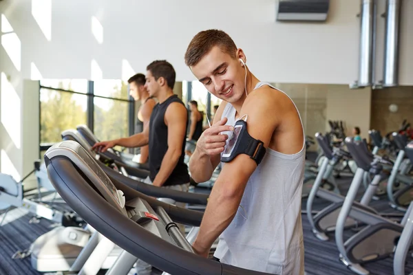 Hombre con smartphone haciendo ejercicio en la cinta de correr en el gimnasio —  Fotos de Stock