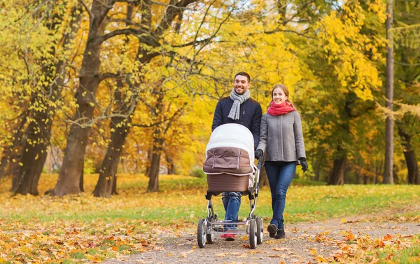 Smiling couple with baby pram in autumn park — Stock Photo, Image