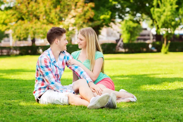 Leende paret sitter på gräset i parken — Stockfoto