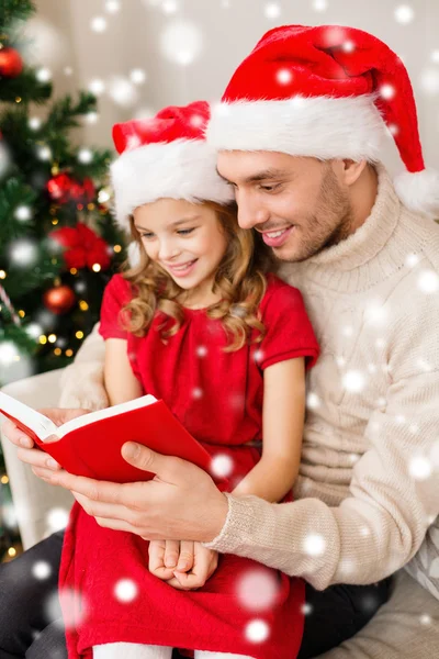 Sorrindo pai e menina em santa chapéus livro de leitura — Fotografia de Stock