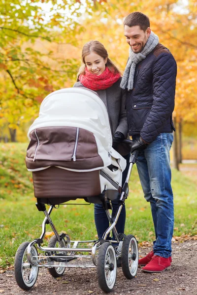 Smiling couple with baby pram in autumn park — Stock Photo, Image