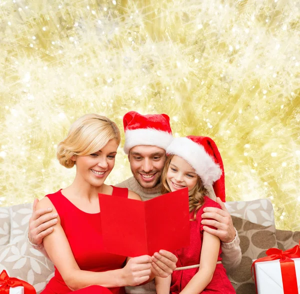 Familia feliz en sombreros de santa con tarjeta de felicitación —  Fotos de Stock