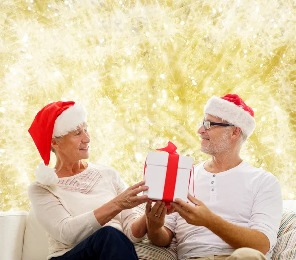 Felice coppia di anziani in cappelli di Babbo Natale con scatola regalo — Foto Stock