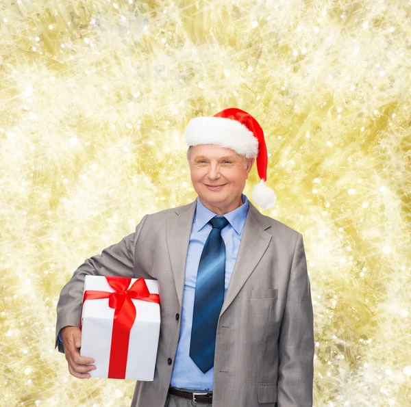 Takım elbise ve santa yardımcı şapkalı hediye ile gülümseyen adam — Stok fotoğraf