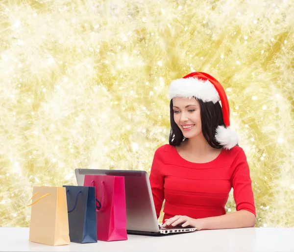 Donna sorridente in cappello di Babbo Natale con borse e laptop — Foto Stock