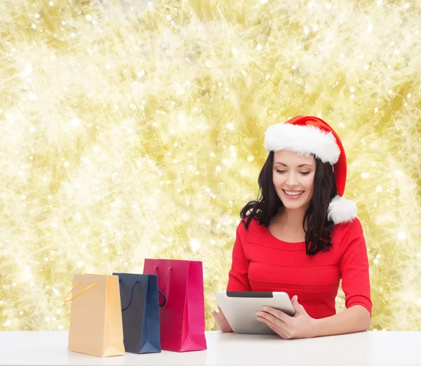 Smiling woman in santa hat with bags and tablet pc — Stock Photo, Image