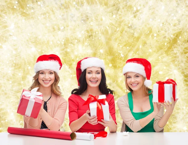 Lächelnde Frauen in Weihnachtsmannhüten, die Geschenke einpacken — Stockfoto