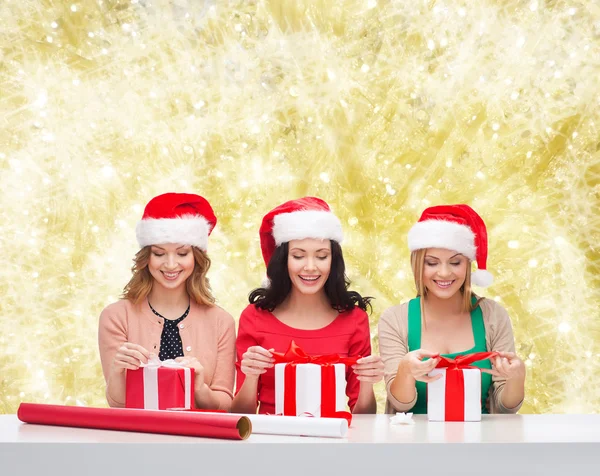 Donne sorridenti in cappelli Babbo Natale helper imballaggio regali — Foto Stock