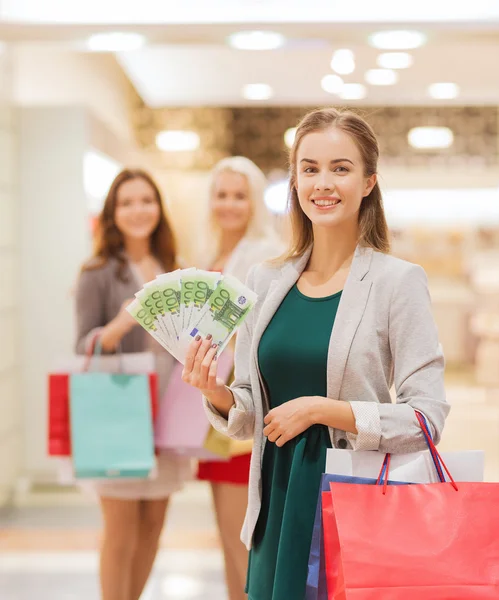 Mujeres jóvenes con bolsas de compras y dinero en el centro comercial —  Fotos de Stock