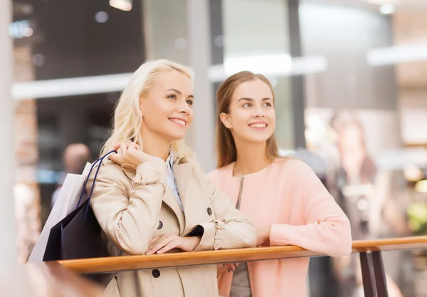 Glada unga kvinnor med shoppingkassar i gallerian — Stockfoto