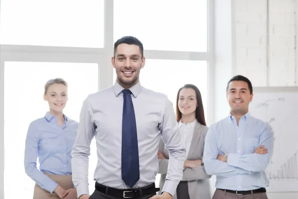 Empresário sorridente no cargo com equipe nas costas — Fotografia de Stock