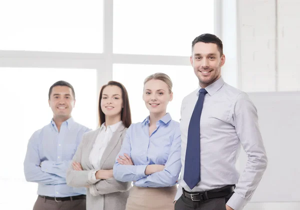 Empresário sorridente no cargo com equipe nas costas — Fotografia de Stock