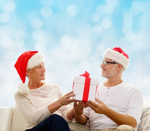 Felice coppia di anziani in cappelli di Babbo Natale con scatola regalo — Foto Stock