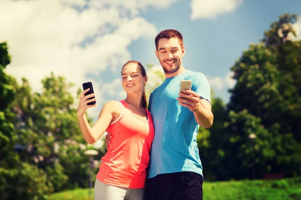 Dos personas sonrientes con teléfonos inteligentes al aire libre —  Fotos de Stock