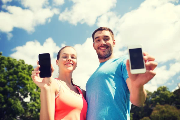 Två leende människor med smartphones utomhus — Stockfoto