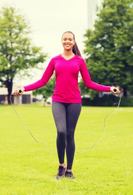 smiling woman exercising with jump-rope outdoors clipart