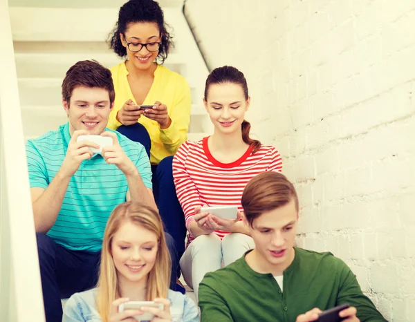 Estudiantes sonrientes con mensajes de texto de teléfonos inteligentes en la escuela — Foto de Stock