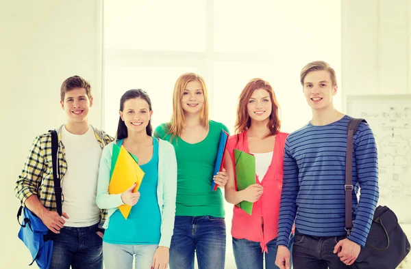 Smiling students with bags and folders at school — Stock Photo, Image