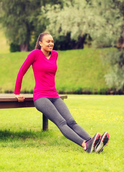 Sonriente mujer haciendo flexiones en el banco al aire libre — Foto de Stock