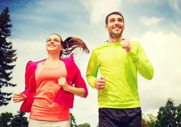 Sonriente pareja con auriculares corriendo al aire libre — Foto de Stock