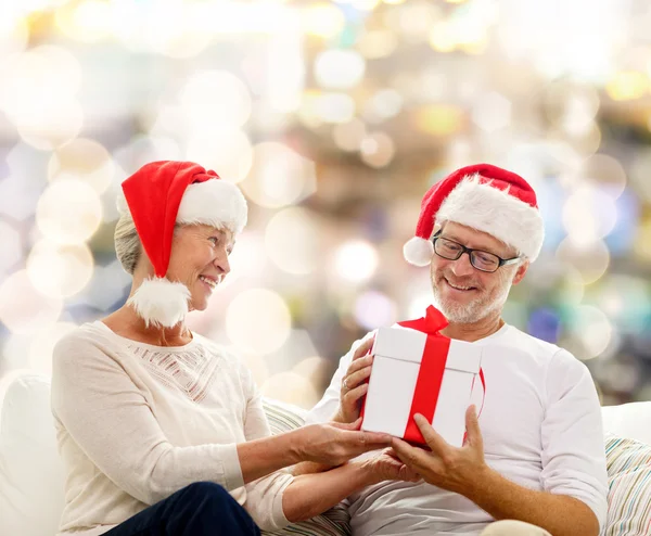 Felice coppia di anziani in cappelli di Babbo Natale con scatola regalo — Foto Stock