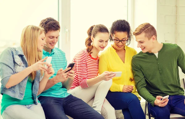 Studenti sorridenti con messaggi di smartphone a scuola — Foto Stock