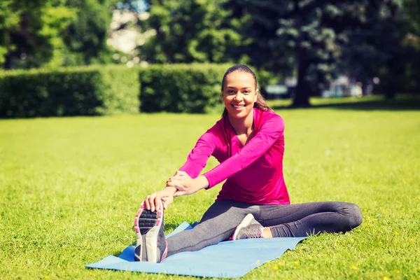 Lächelnde Frau streckt Bein auf Matte im Freien — Stockfoto