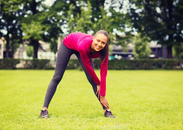Smiling black woman stretching leg outdoors — Stock Photo, Image