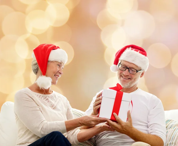 Feliz pareja de ancianos en sombreros de santa con caja de regalo — Foto de Stock