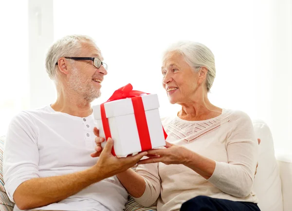 Feliz pareja de ancianos con caja de regalo en casa — Foto de Stock