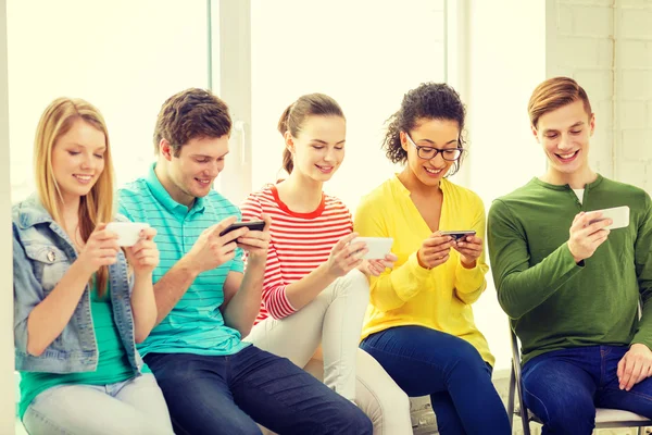 Smiling students with smartphone texting at school — Stock Photo, Image