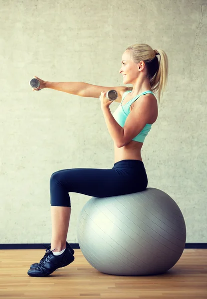 Улыбающаяся женщина с гантелями и мячом для упражнений — стоковое фото
