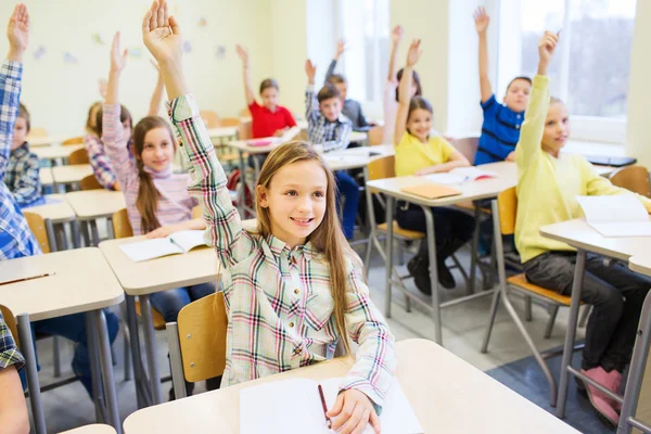 Grupo de crianças da escola levantando as mãos em sala de aula — Fotografia de Stock