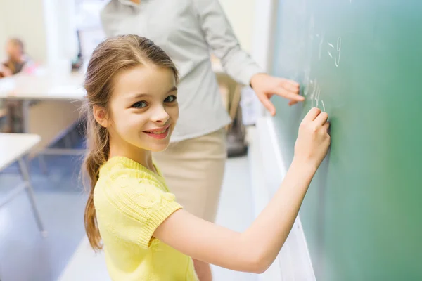 Kleines lächelndes Schulmädchen schreibt auf Kreidetafel — Stockfoto