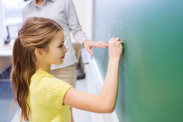 Malé usmívající se školačka psaní na tabuli křídou — Stock fotografie