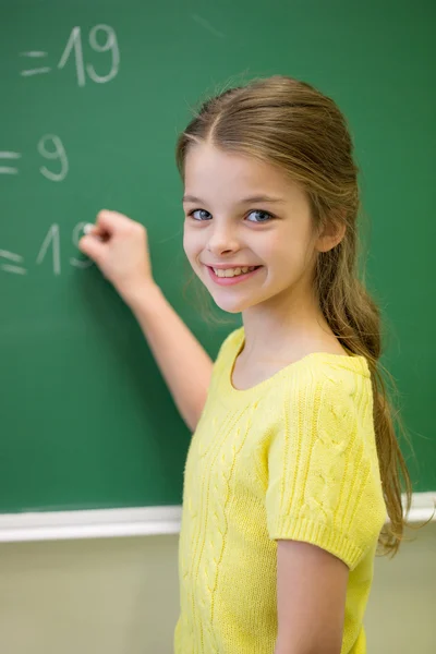 Kleines lächelndes Schulmädchen schreibt auf Kreidetafel — Stockfoto