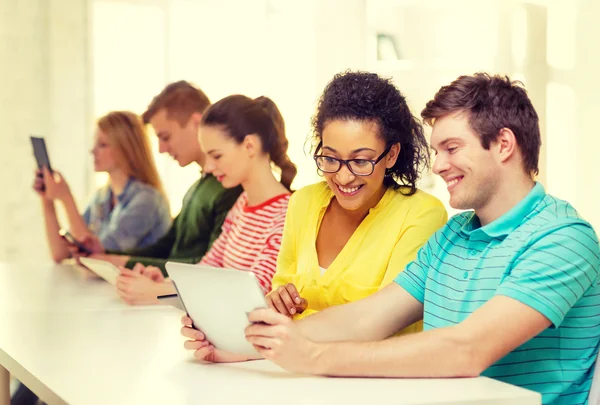 Lachende studenten kijken naar tablet pc op school — Stockfoto