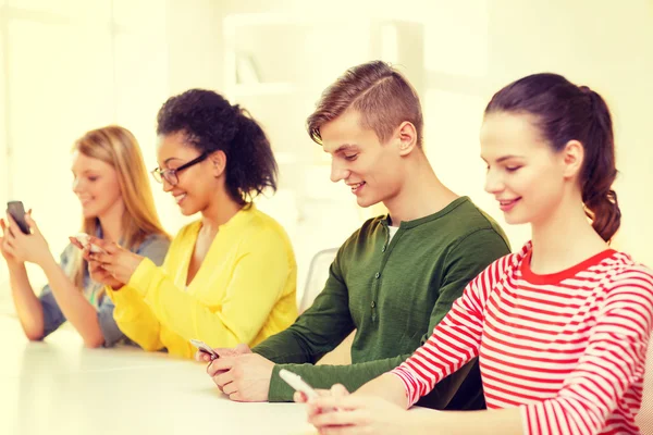 Cuatro estudiantes sonrientes con smartphones en la escuela Imagen De Stock