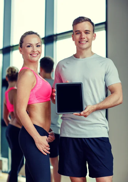 Smiling young woman with personal trainer in gym — Stock Photo, Image