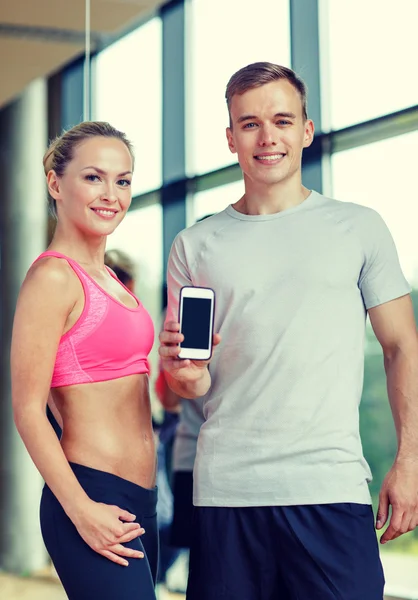 Giovane donna sorridente con personal trainer in palestra — Foto Stock